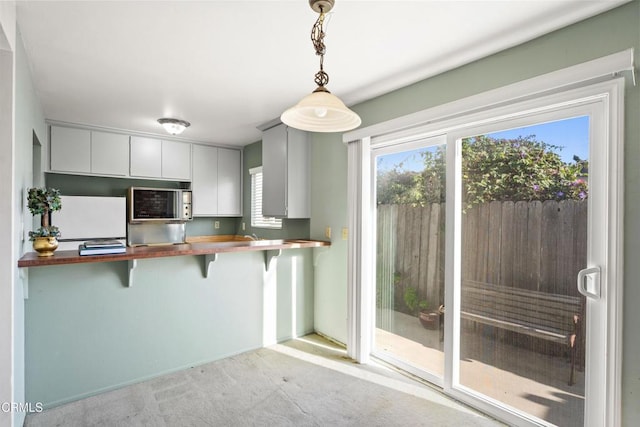 kitchen featuring pendant lighting, white refrigerator, light colored carpet, a kitchen bar, and butcher block counters