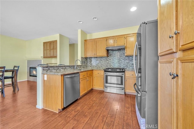 kitchen featuring light stone counters, kitchen peninsula, wood-type flooring, decorative backsplash, and appliances with stainless steel finishes