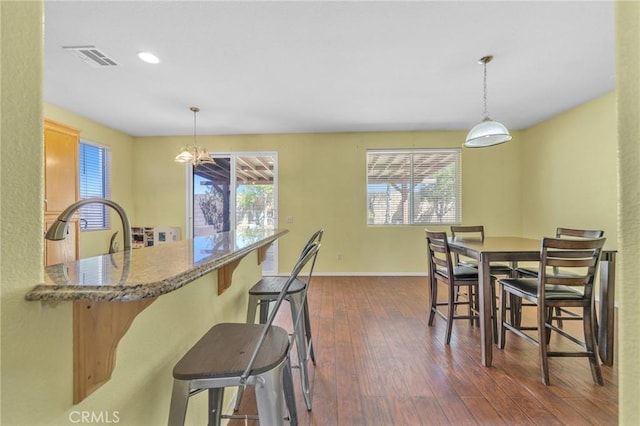 kitchen featuring a breakfast bar area, light stone counters, dark hardwood / wood-style flooring, and pendant lighting