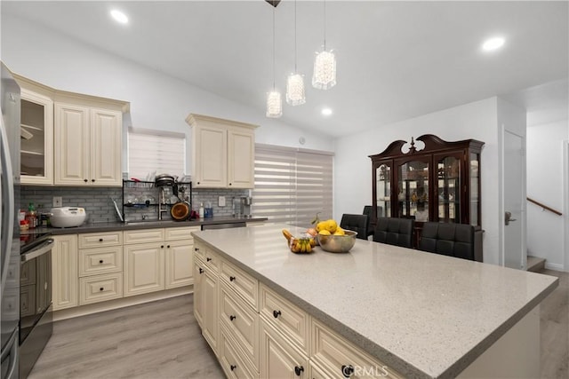 kitchen featuring lofted ceiling, backsplash, cream cabinets, decorative light fixtures, and light hardwood / wood-style floors