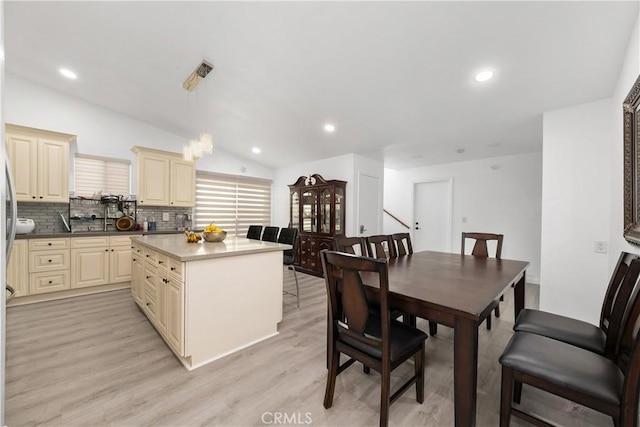 kitchen featuring backsplash, vaulted ceiling, cream cabinets, decorative light fixtures, and light hardwood / wood-style flooring