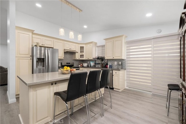 kitchen with stainless steel appliances, cream cabinets, a center island, light hardwood / wood-style floors, and hanging light fixtures