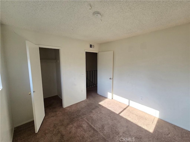 unfurnished bedroom featuring dark carpet, a textured ceiling, and a closet