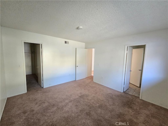 unfurnished bedroom with a textured ceiling, a spacious closet, light carpet, and a closet