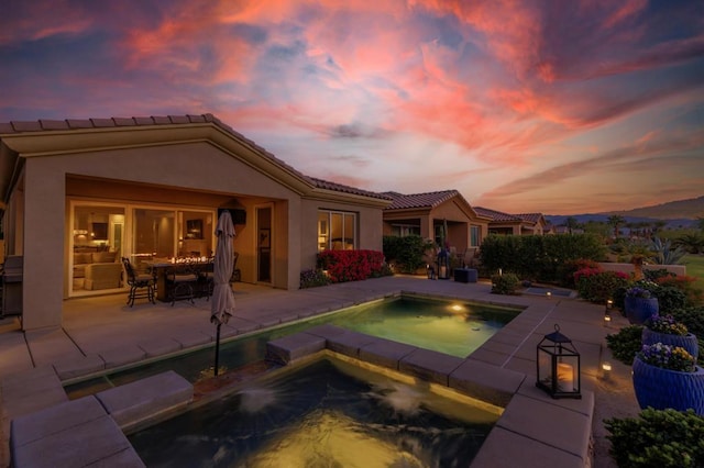 pool at dusk featuring an in ground hot tub and a patio