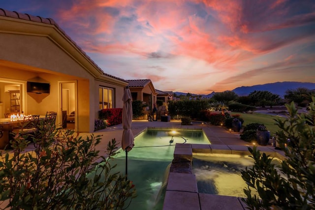 pool at dusk with a mountain view, an in ground hot tub, and a patio