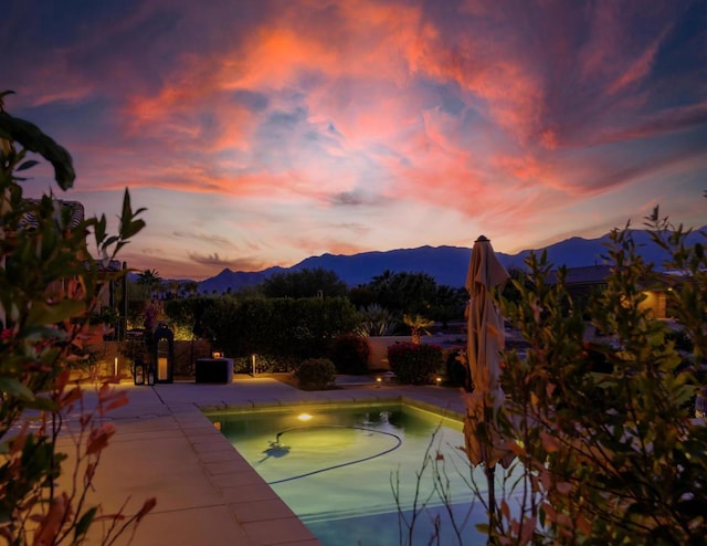 pool at dusk featuring a mountain view and a patio