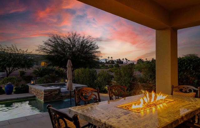 patio terrace at dusk featuring a swimming pool with hot tub and an outdoor fire pit