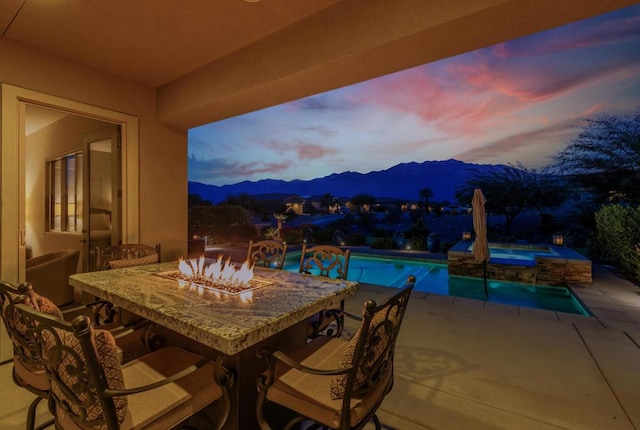 patio terrace at dusk with a mountain view, a pool with hot tub, and an outdoor fire pit