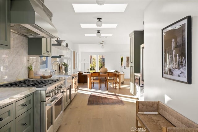 kitchen featuring green cabinets, range with two ovens, a skylight, wall chimney exhaust hood, and wood-type flooring