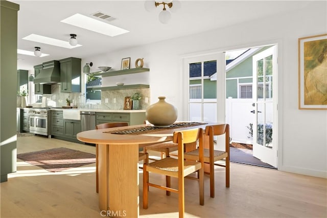 dining room featuring a skylight, french doors, and light wood-type flooring