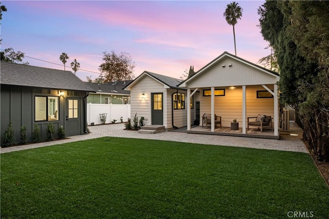 back house at dusk featuring a lawn and a patio