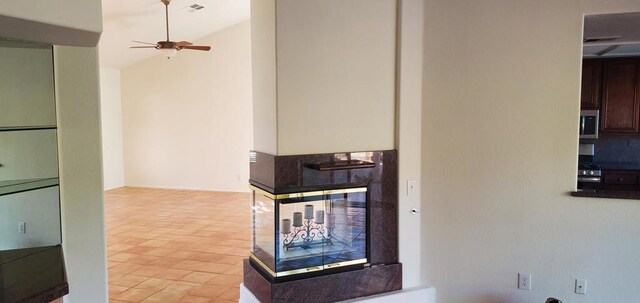 unfurnished living room with light tile patterned flooring, lofted ceiling, a multi sided fireplace, and ceiling fan