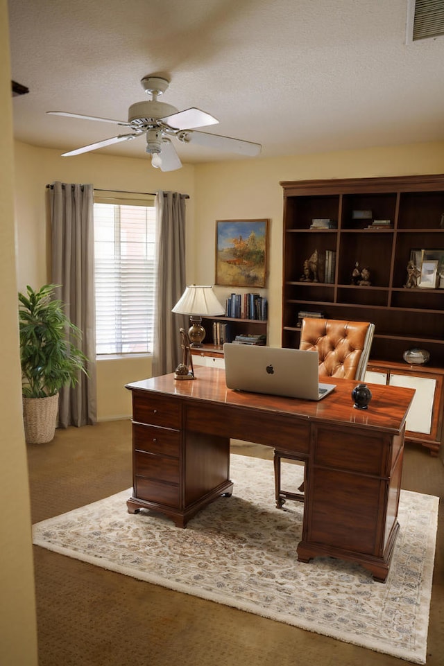 carpeted home office with ceiling fan and a textured ceiling