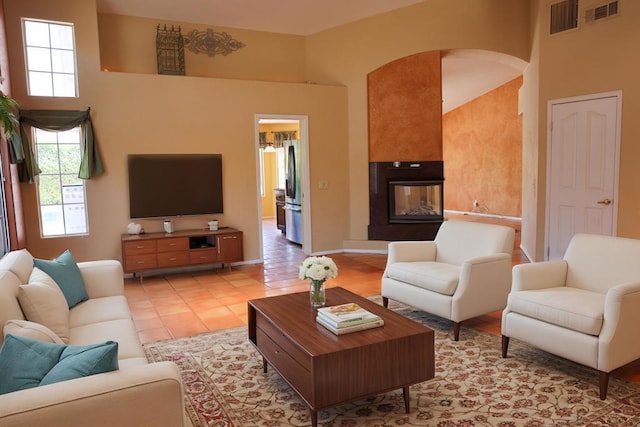 tiled living room with a multi sided fireplace and a towering ceiling