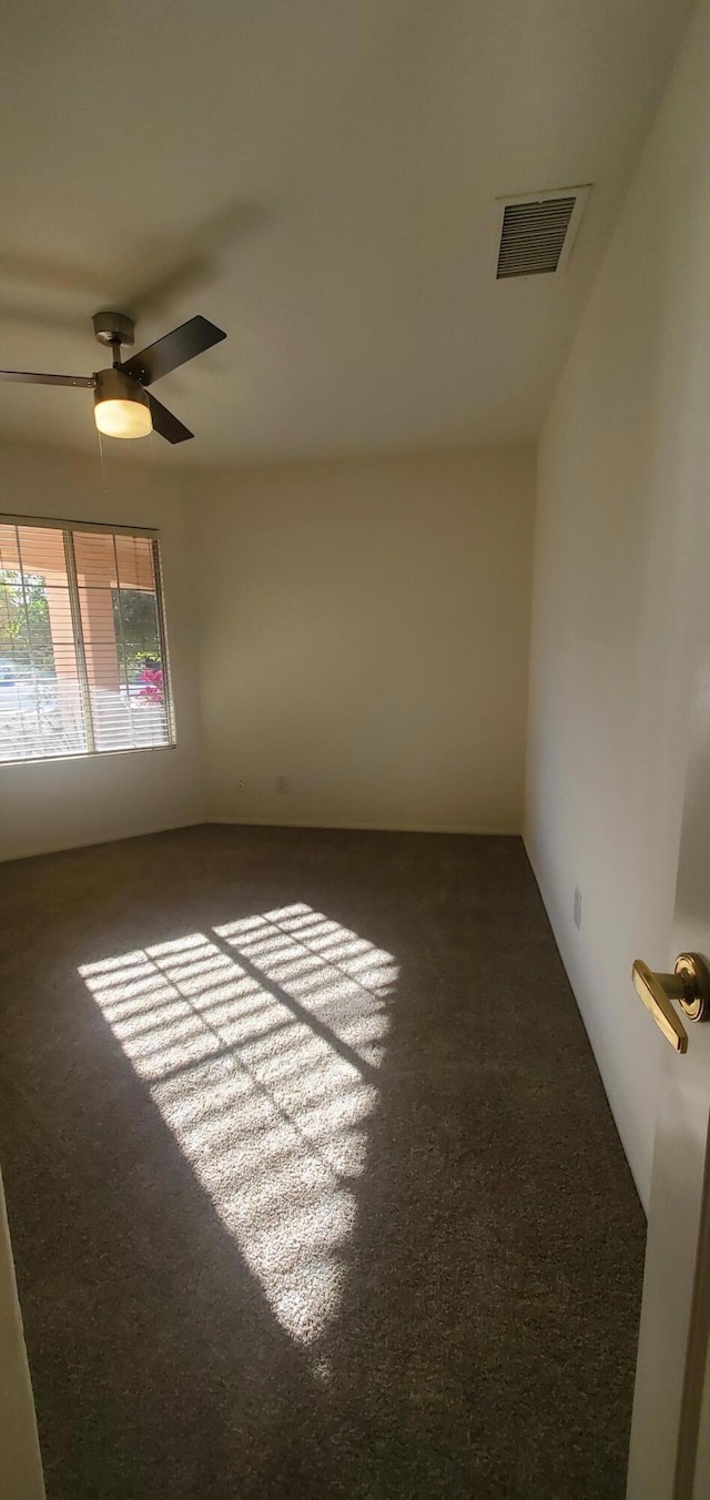 empty room featuring ceiling fan and dark colored carpet