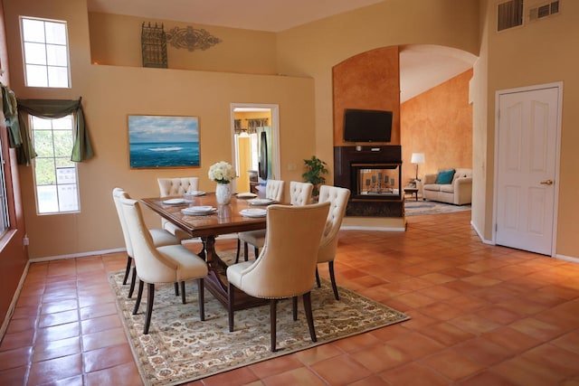 dining area featuring a multi sided fireplace, tile patterned floors, and a high ceiling