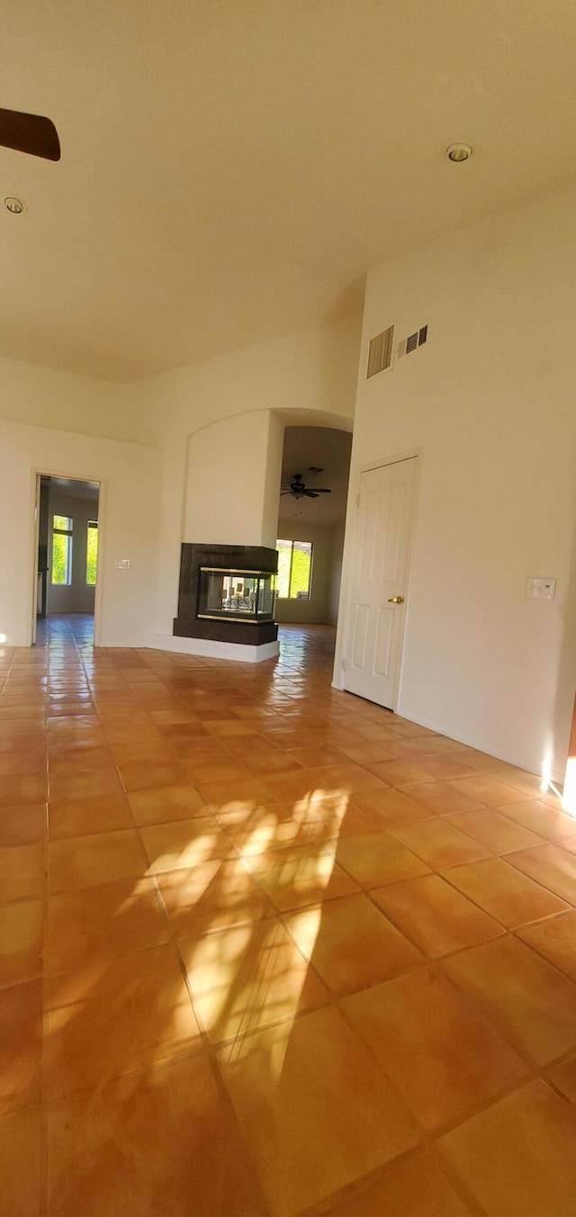 unfurnished living room with tile patterned flooring, ceiling fan, and a multi sided fireplace