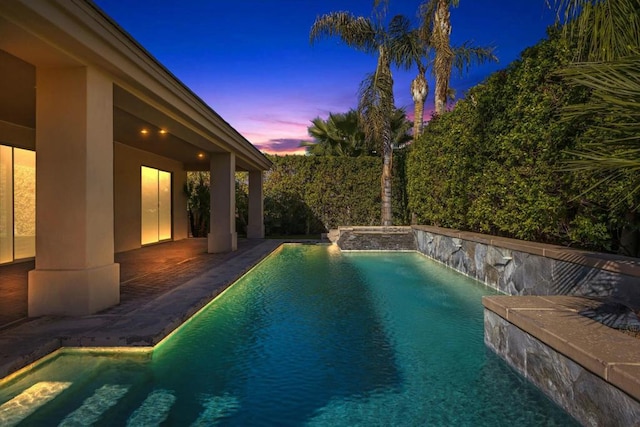 pool at dusk featuring pool water feature