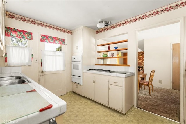 kitchen featuring white cabinetry, tile countertops, stainless steel gas cooktop, oven, and sink