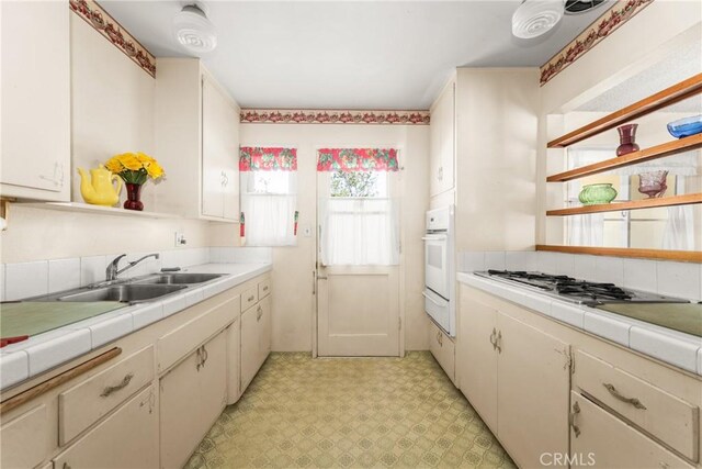 kitchen with stainless steel gas stovetop, oven, sink, white cabinetry, and tile counters