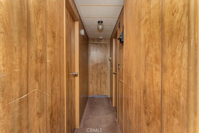 hallway featuring wood walls and dark colored carpet