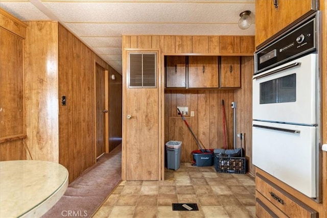 kitchen featuring wood walls, white double oven, and light carpet