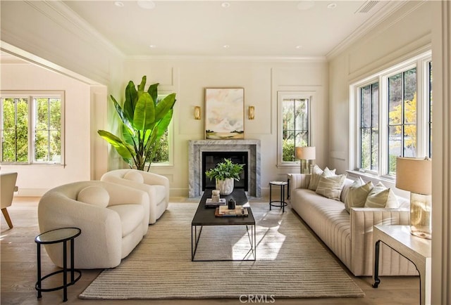 living room with light wood-type flooring, a fireplace, a wealth of natural light, and ornamental molding