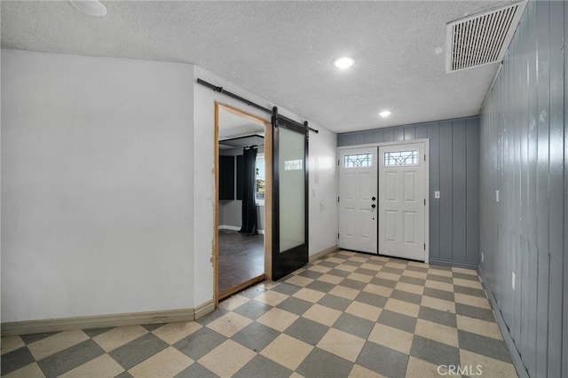 foyer with a barn door, wooden walls, and a textured ceiling