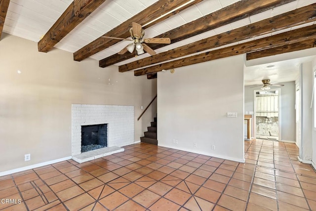 unfurnished living room featuring ceiling fan, a brick fireplace, dark tile patterned floors, and beam ceiling