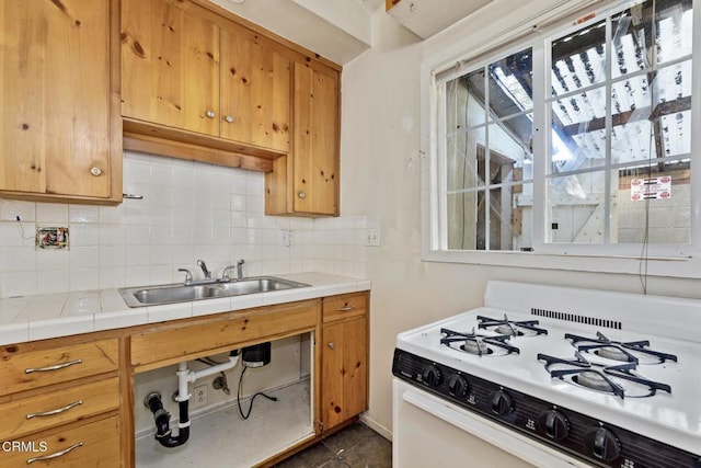 kitchen featuring gas range gas stove, tile countertops, backsplash, sink, and dark tile patterned floors