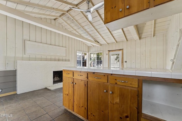 kitchen with dark tile patterned floors, tile counters, wood ceiling, lofted ceiling with beams, and a brick fireplace