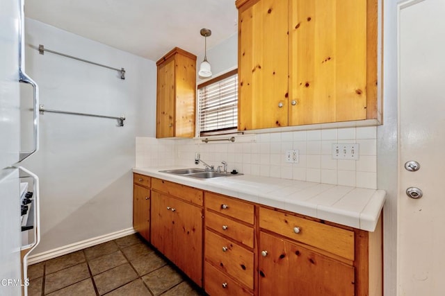 kitchen featuring decorative light fixtures, dark tile patterned flooring, tile countertops, decorative backsplash, and sink