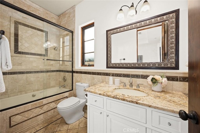 full bathroom featuring vanity, tile patterned floors, combined bath / shower with glass door, toilet, and tile walls