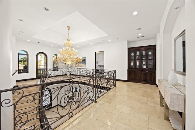 hall with a raised ceiling and a chandelier