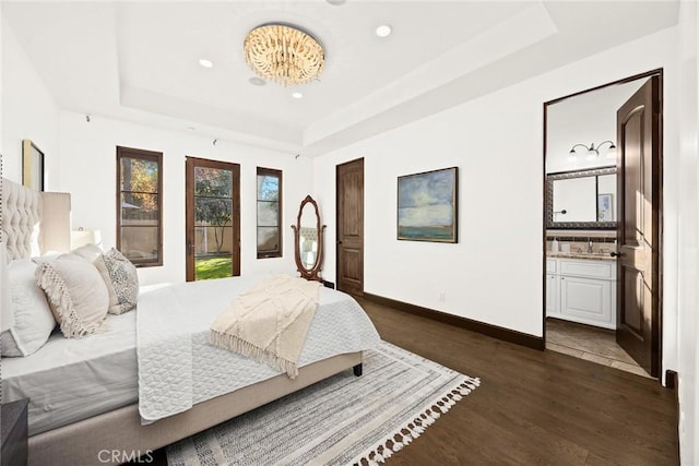 bedroom featuring a tray ceiling, ensuite bath, and dark hardwood / wood-style flooring