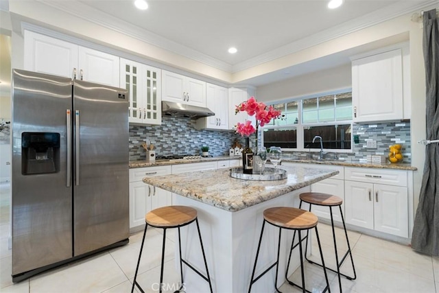 kitchen featuring light stone countertops, a center island, a breakfast bar area, white cabinets, and appliances with stainless steel finishes