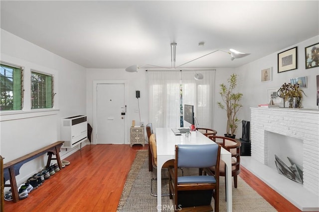 dining space featuring heating unit, a wealth of natural light, light hardwood / wood-style flooring, and a brick fireplace