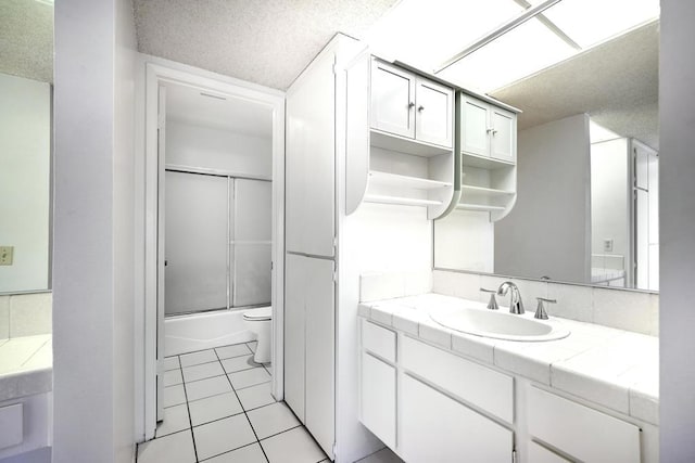 full bathroom featuring tile patterned flooring, toilet, vanity, bath / shower combo with glass door, and a textured ceiling