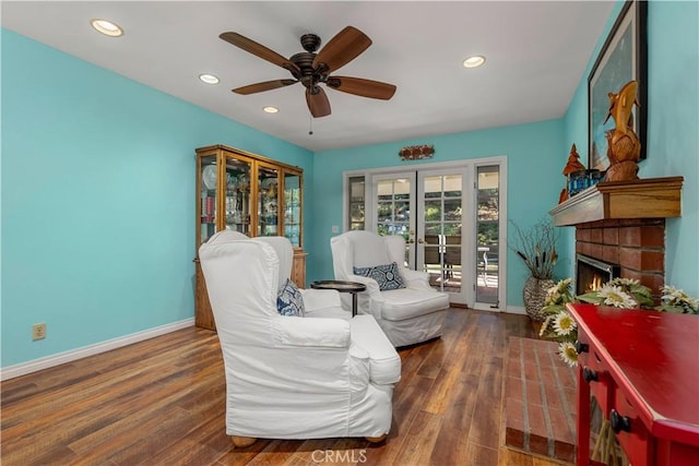 living area with ceiling fan, dark hardwood / wood-style flooring, french doors, and a brick fireplace