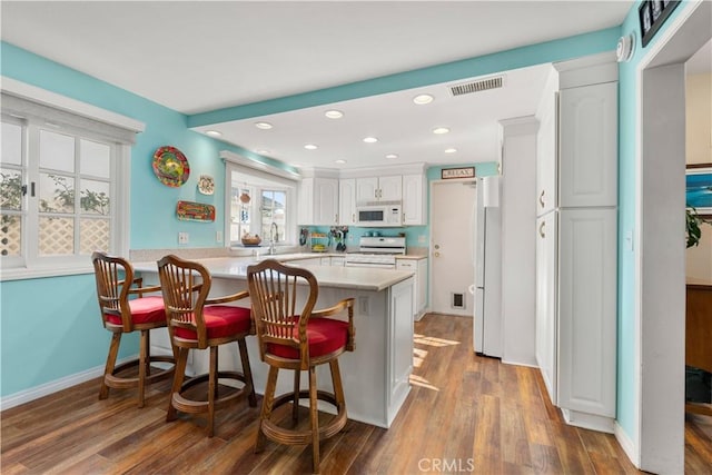 kitchen with white appliances, wood-type flooring, white cabinetry, kitchen peninsula, and a breakfast bar area