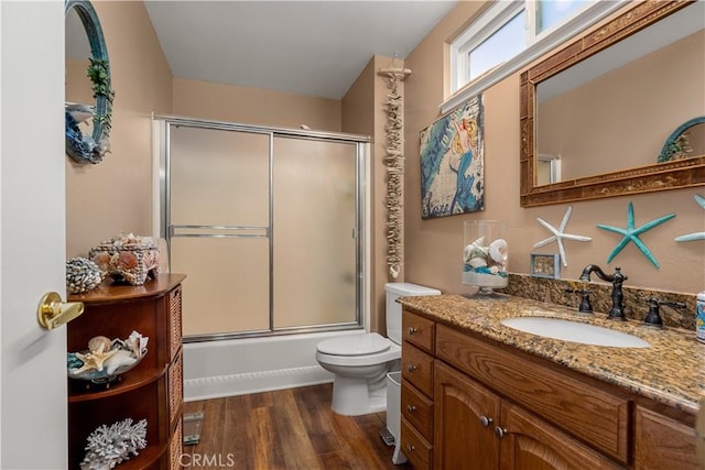 full bathroom featuring hardwood / wood-style flooring, combined bath / shower with glass door, vanity, and toilet