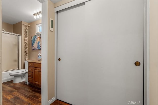 full bathroom with wood-type flooring, combined bath / shower with glass door, vanity, and toilet