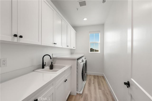 laundry room featuring washing machine and dryer, sink, cabinets, and light hardwood / wood-style floors