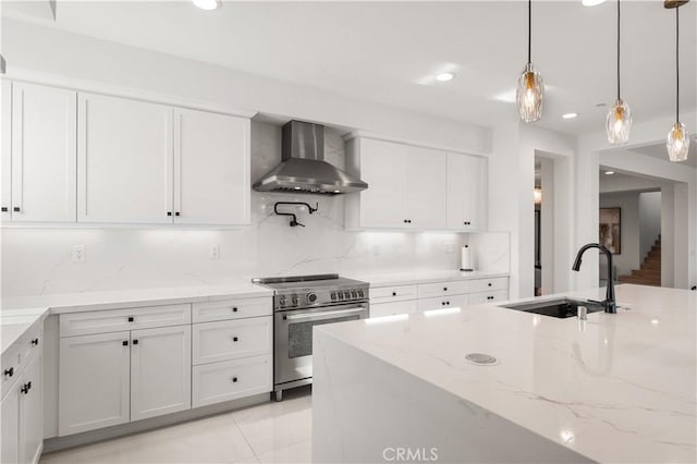 kitchen with white cabinets, wall chimney range hood, hanging light fixtures, sink, and stainless steel stove