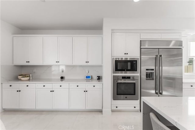 kitchen with built in appliances, light stone countertops, and white cabinets