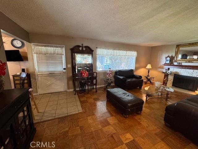 living room with a textured ceiling, a stone fireplace, and parquet floors