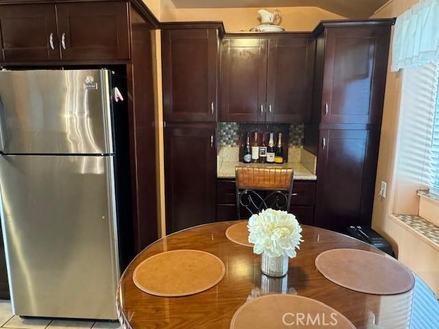 kitchen featuring decorative backsplash, light tile patterned floors, dark brown cabinetry, and stainless steel refrigerator