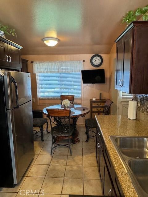 kitchen featuring sink, stainless steel fridge, dark brown cabinets, light tile patterned flooring, and light stone counters