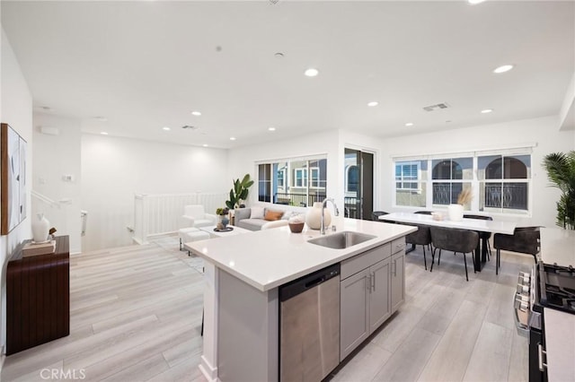 kitchen with light hardwood / wood-style floors, a center island with sink, gray cabinets, dishwasher, and sink